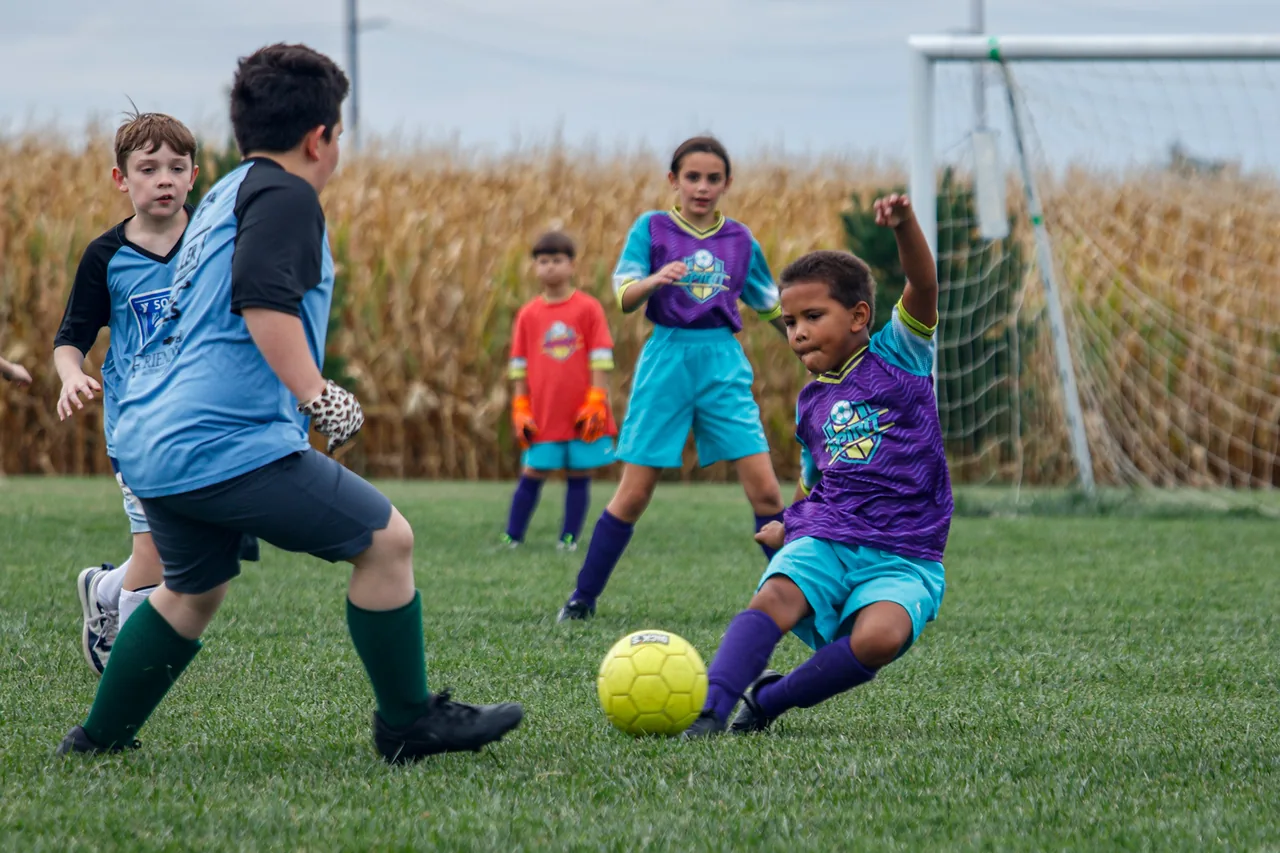 A soccer player extends a leg toward a yellow ball from a low position on the grass.