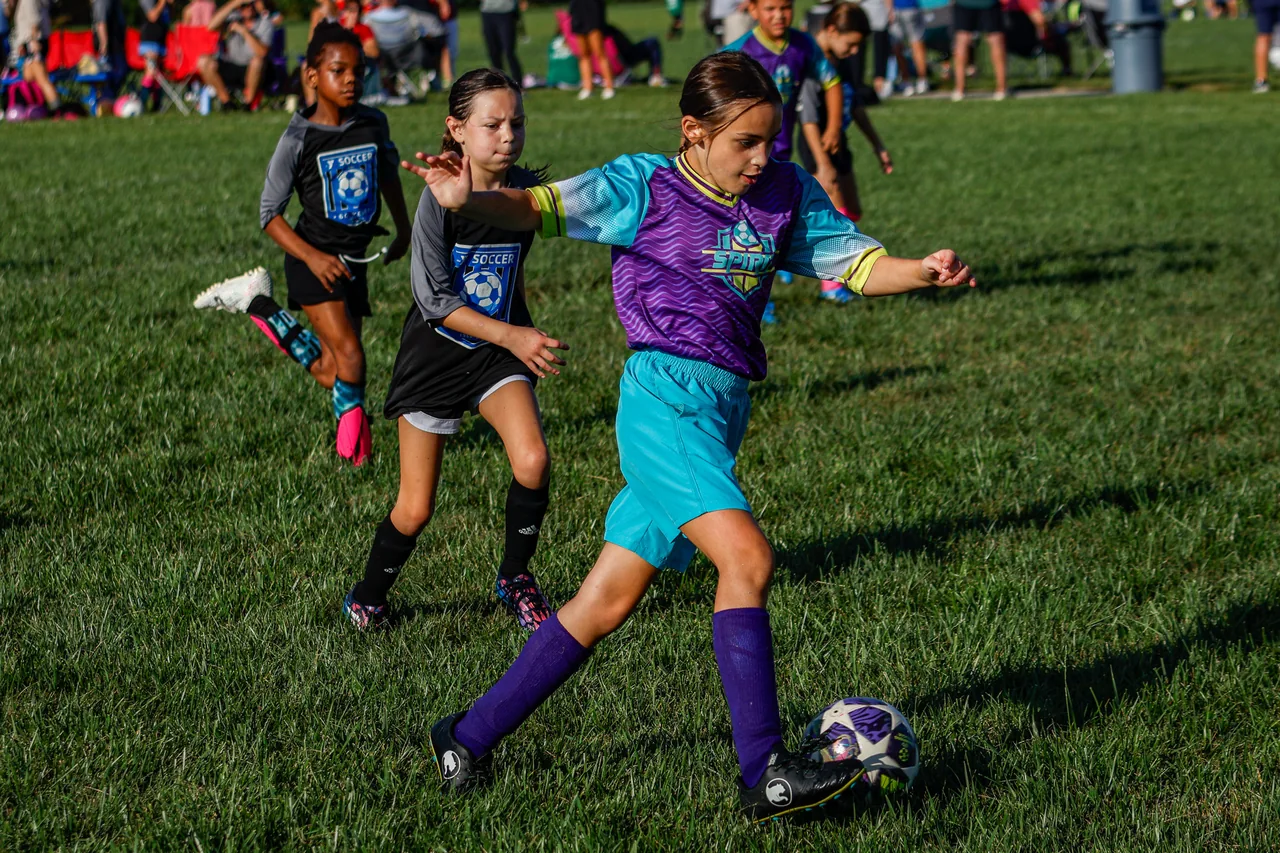 A soccer player in purple carries the ball forward as defenders pursue.