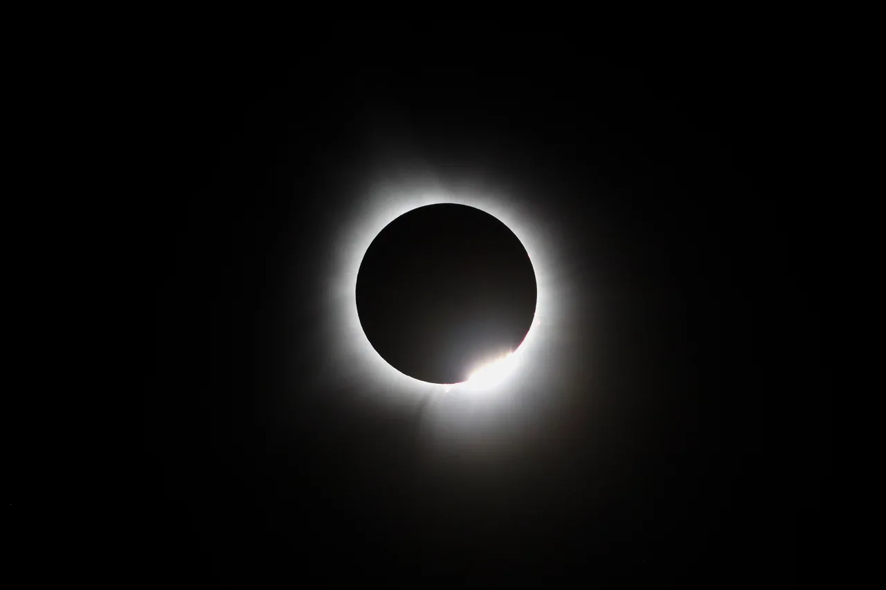 The moon eclipses the sun, with a bright diamond ring of light along its edge.