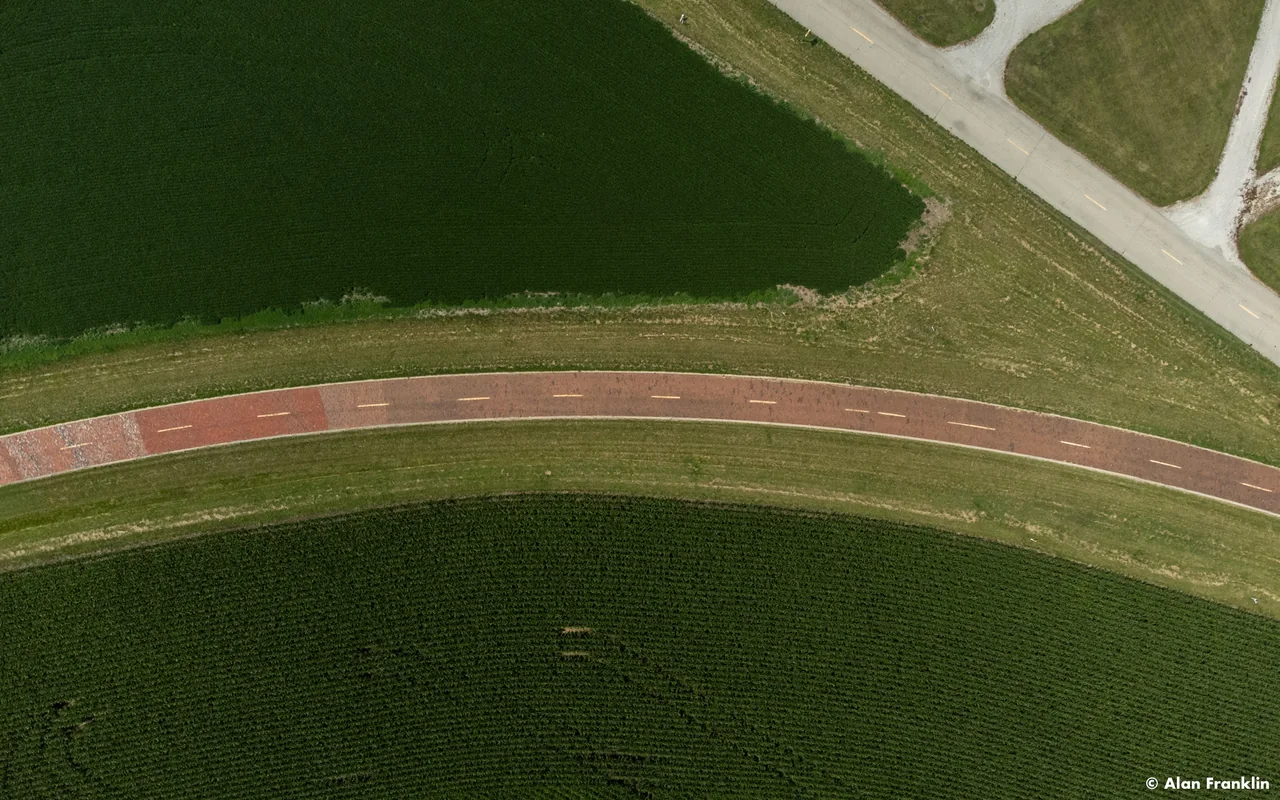A red path arcs between green water and farmland, seen from directly above.